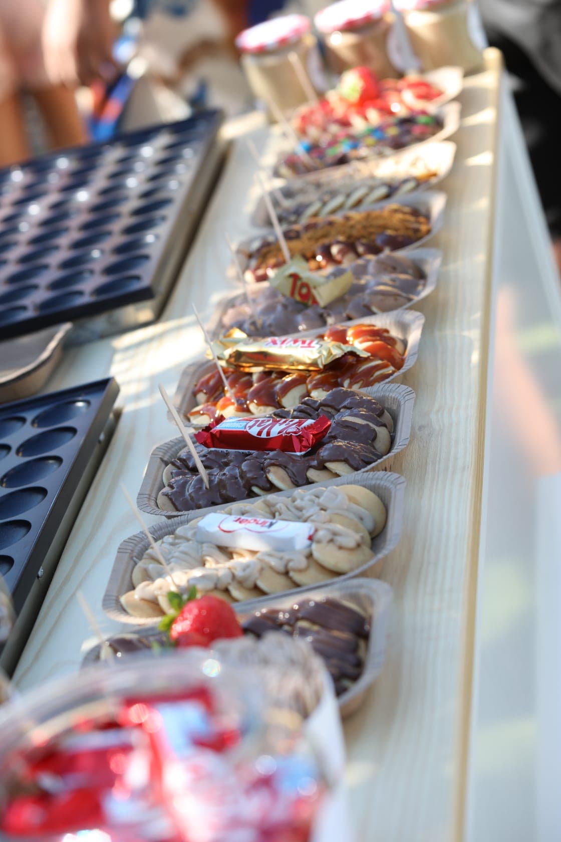 Fila de tabuleiros de mini panquecas com toppings variados, prontos para servir num evento